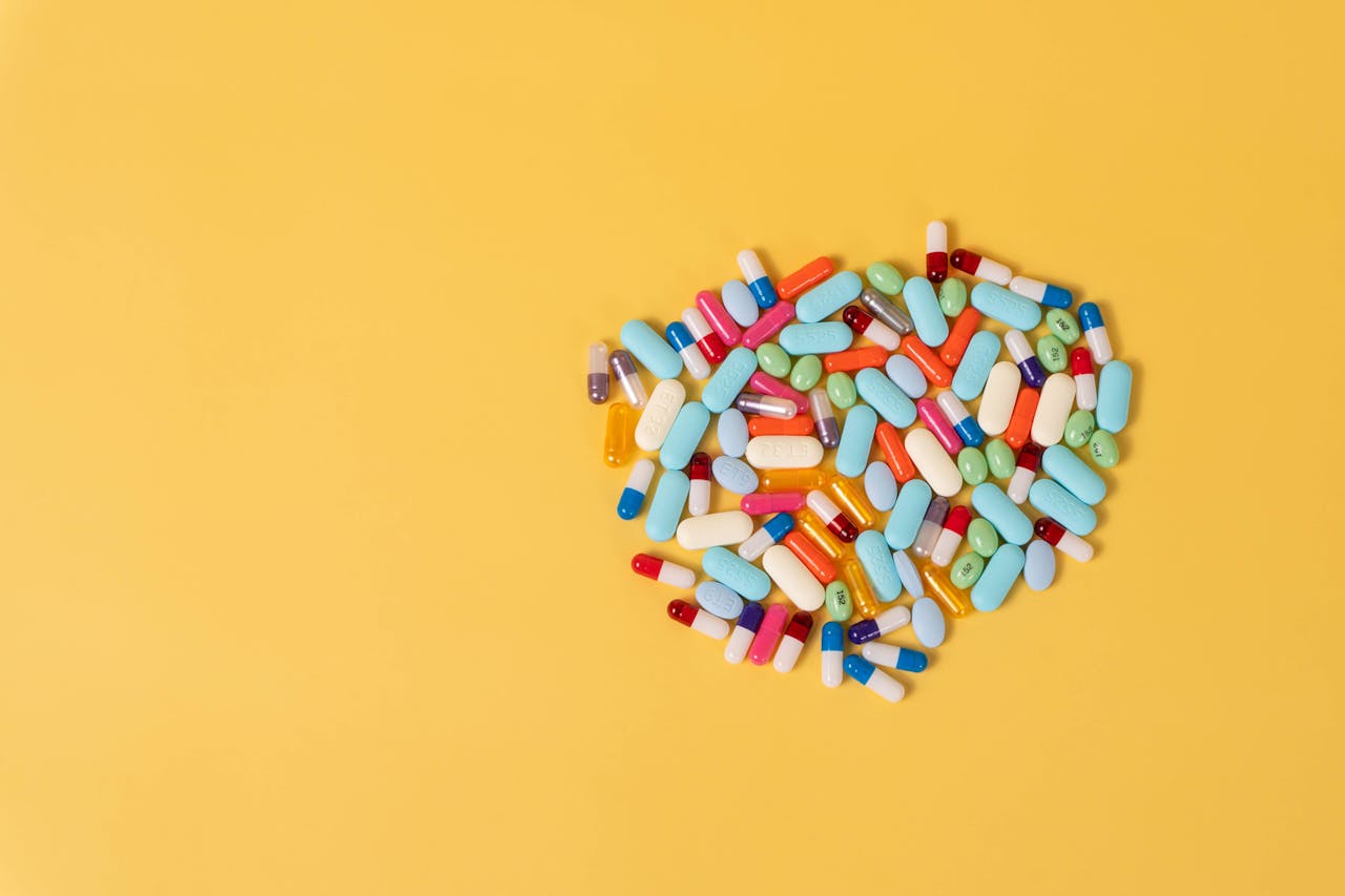 A heart-shaped arrangement of various pills on a vibrant yellow backdrop representing healthcare and medication themes.