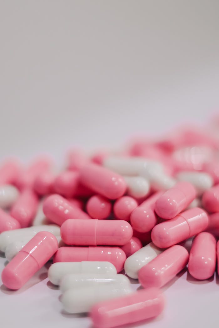 A close-up view of pink and white capsules on a white surface, indicating medication or vitamins.