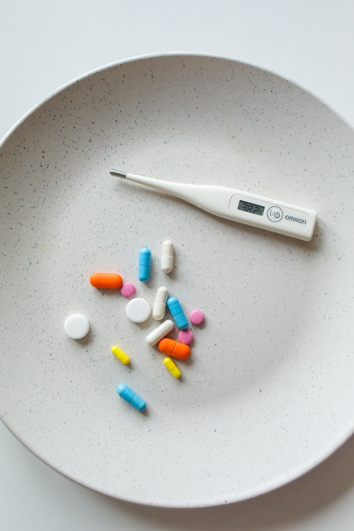 An assortment of colorful pills and a digital thermometer on a white plate, symbolizing healthcare and medication.