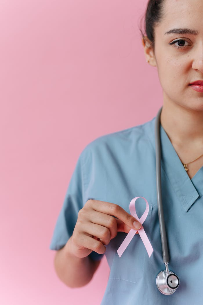 Healthcare worker in medical uniform with a pink ribbon for breast cancer awareness.